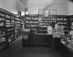 Inside of Everly Drug Store, view of the cash register surrounded by shelves of medicine, hygienic products, beauty products, etc. by William Garber