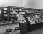 Inside Everly Drug Store, view of one end of the soda counter next to a display of greeting cards, books, etc. by William Garber