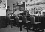 Inside of Quedens Lunch Billiards, New Market, Va. Front view of the counter, with two men standing underneath the menu. by William Garber