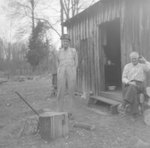 Two men posing outside of a wooden shed or shack by William Garber