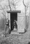 Two men in suits, one sitting inside of an outhouse on the toilet, and the other leaning against the outside wall by William Garber