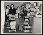 A woman and two children shopping inside of a grocery store. She has Dr. Pepper in her cart, is standing next to a display for Dr. Pepper, and there is a Dr. Pepper delivery man in the background. by William Garber