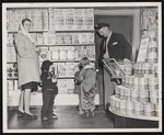 A woman, three young children, and a Dr. Pepper delivery man standing next to a wall of shelves filled with cereals inside of a grocery store by William Garber