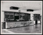 Inside of an automotive store; view of the main counter and cash register, with a small office to the side. Advertisement for Ford auto parts above the counter by William Garber