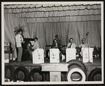 A jazz band called "The Music Mac's" performing on a small wooden stage that is lined with automobile tires by William Garber