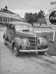 A private automobile parked next to a Coca-Cola advertisement by William Garber