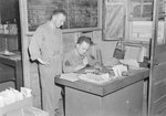 Two men in military uniform, one sitting at a desk and the other looking over his shoulder. by William Garber