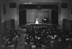 New Market High School, view from the back of the auditorium, where a woman and a man are playing the violin and piano on stage by William Garber