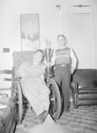 A baseball player of the Timberville Hatchery team posing with a man in a wheelchair and a large trophy by William Garber