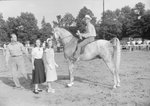Timberville Horse Show, side view of a man riding a horse with a trophy by William Garber