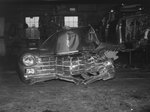 The front-end of a severely damaged car that is sitting inside of a garage or auto shop by William Garber
