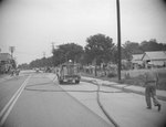 Distant view of a fire engine parked with its water hose stretching across the street by William Garber